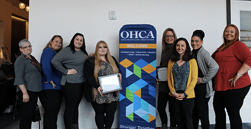 a group of women smiling and standing in front of a banner at the OHCA conference