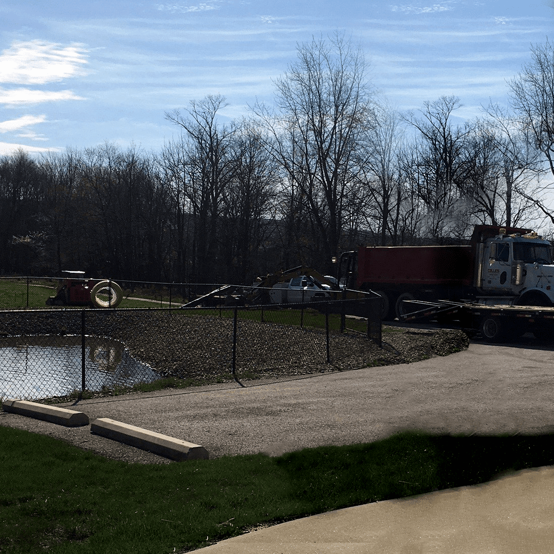 pond with fence around it and construction truck backed up into an open green space